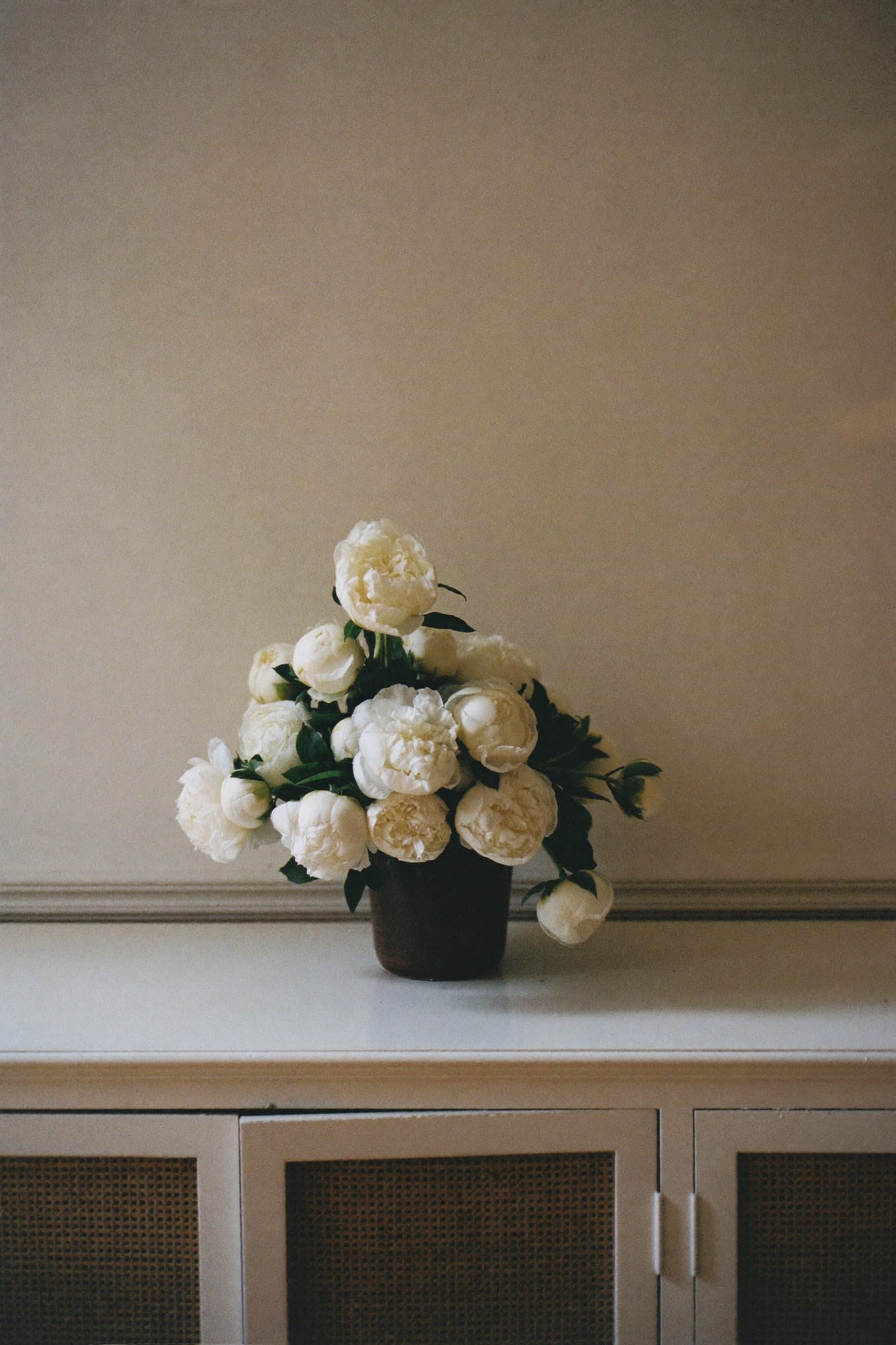 White peonies in a glass vase on a console