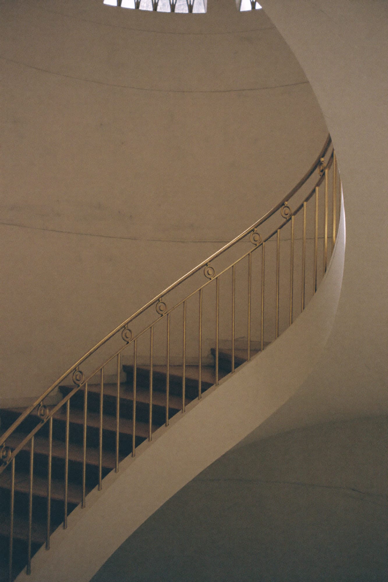A curved staircase with a brass handrail, lit from above