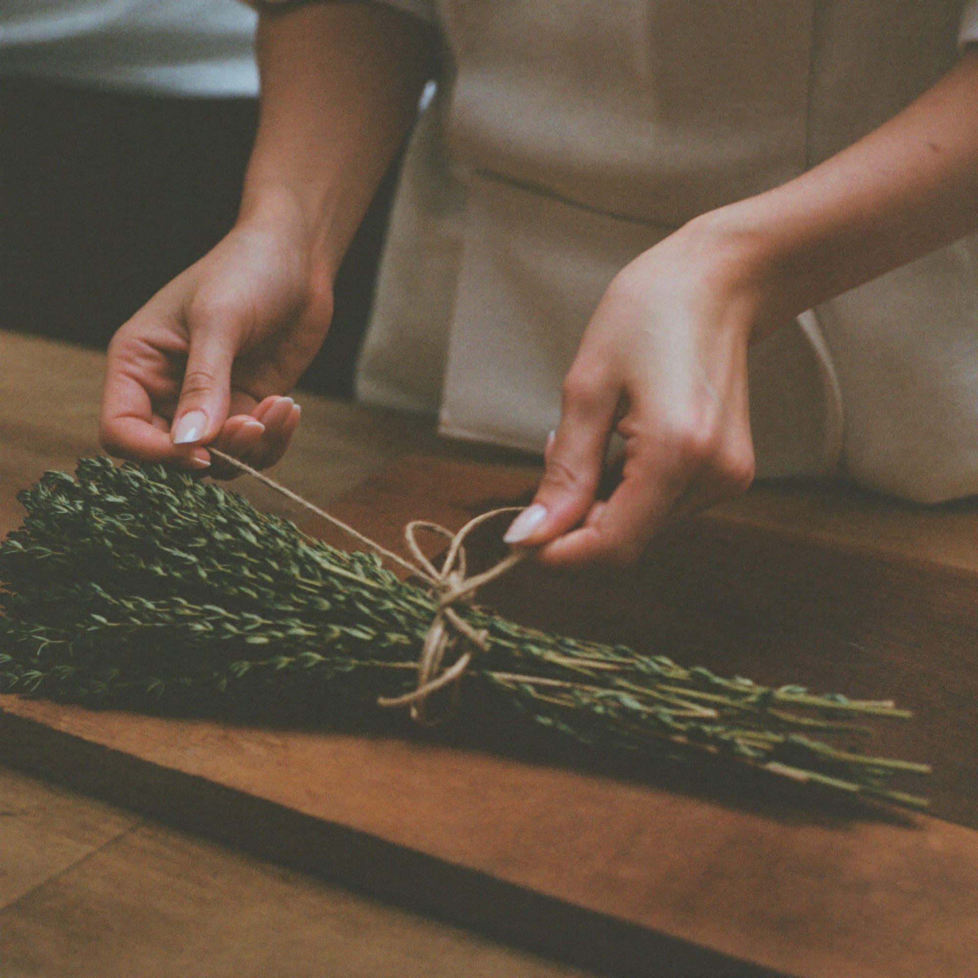 A chef's hands tying thyme with twine on a wooden board