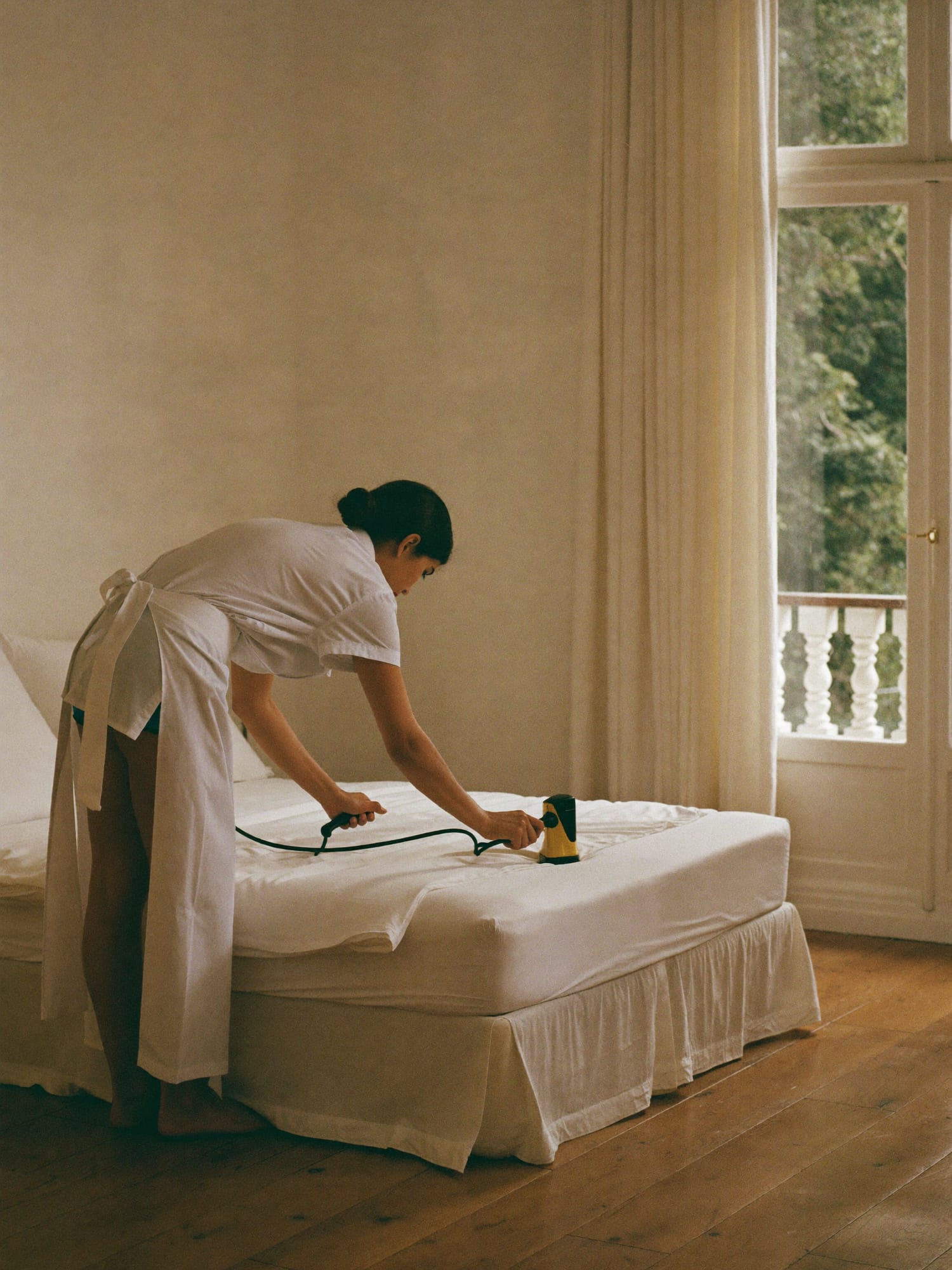 A housekeeper smoothing white linen on a made bed