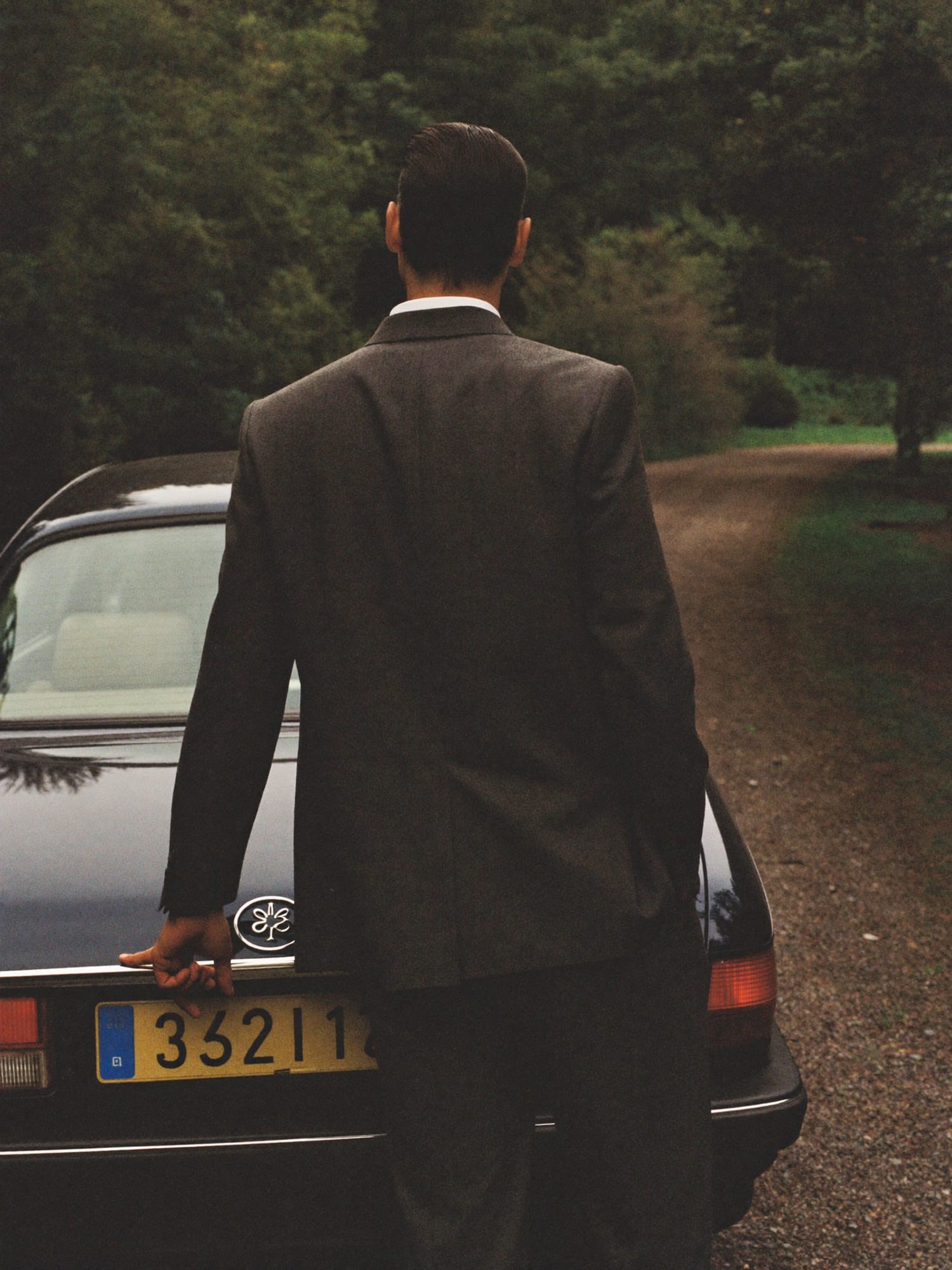 A chauffeur holding open the rear door of a dark saloon