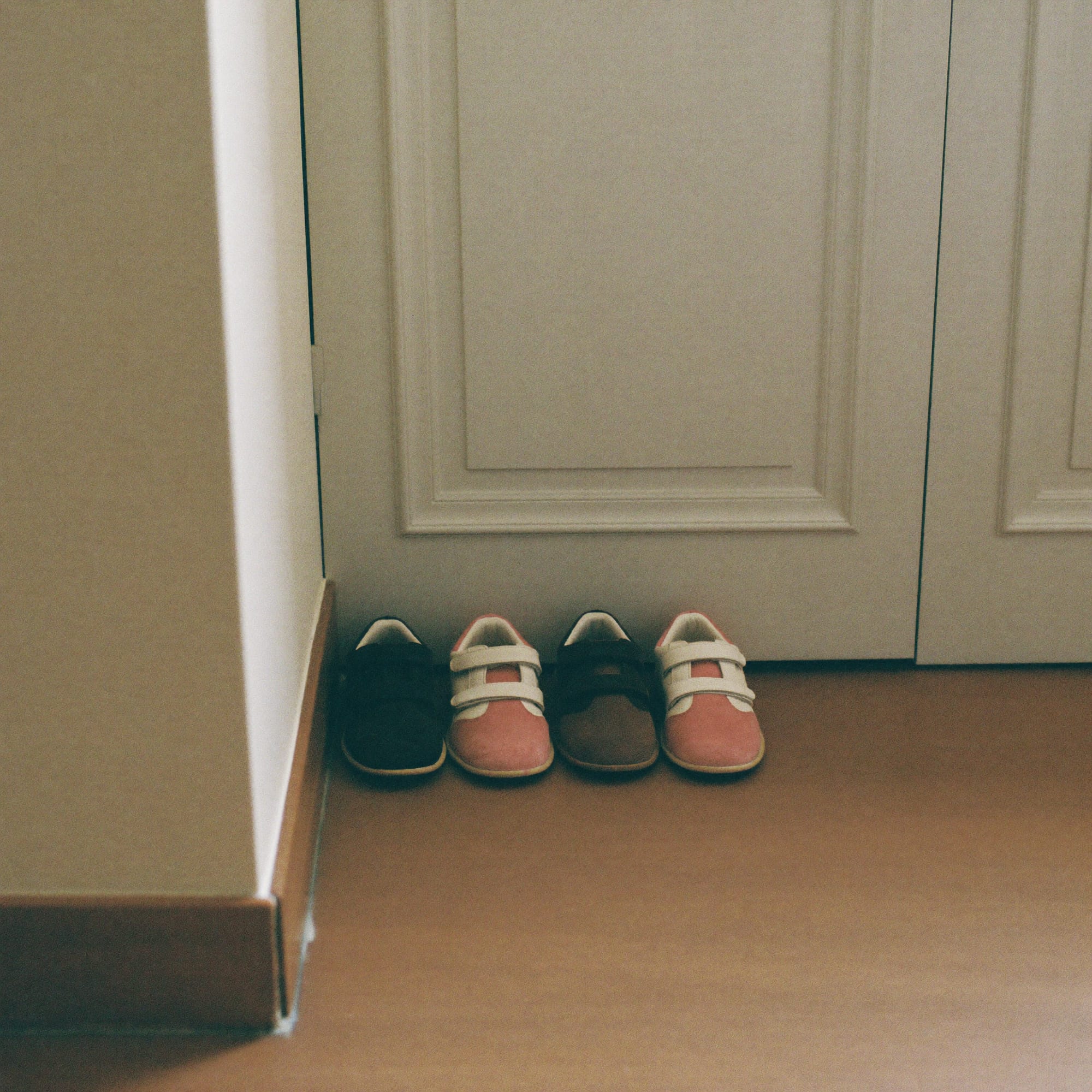 Small children's shoes lined up on a stone floor beside a tall front door