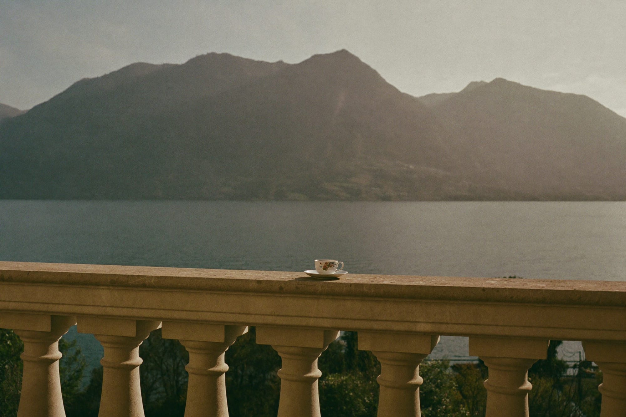 A private terrace above Lake Zürich — an empty sunlit room with a door open to a garden and a sheer curtain moving