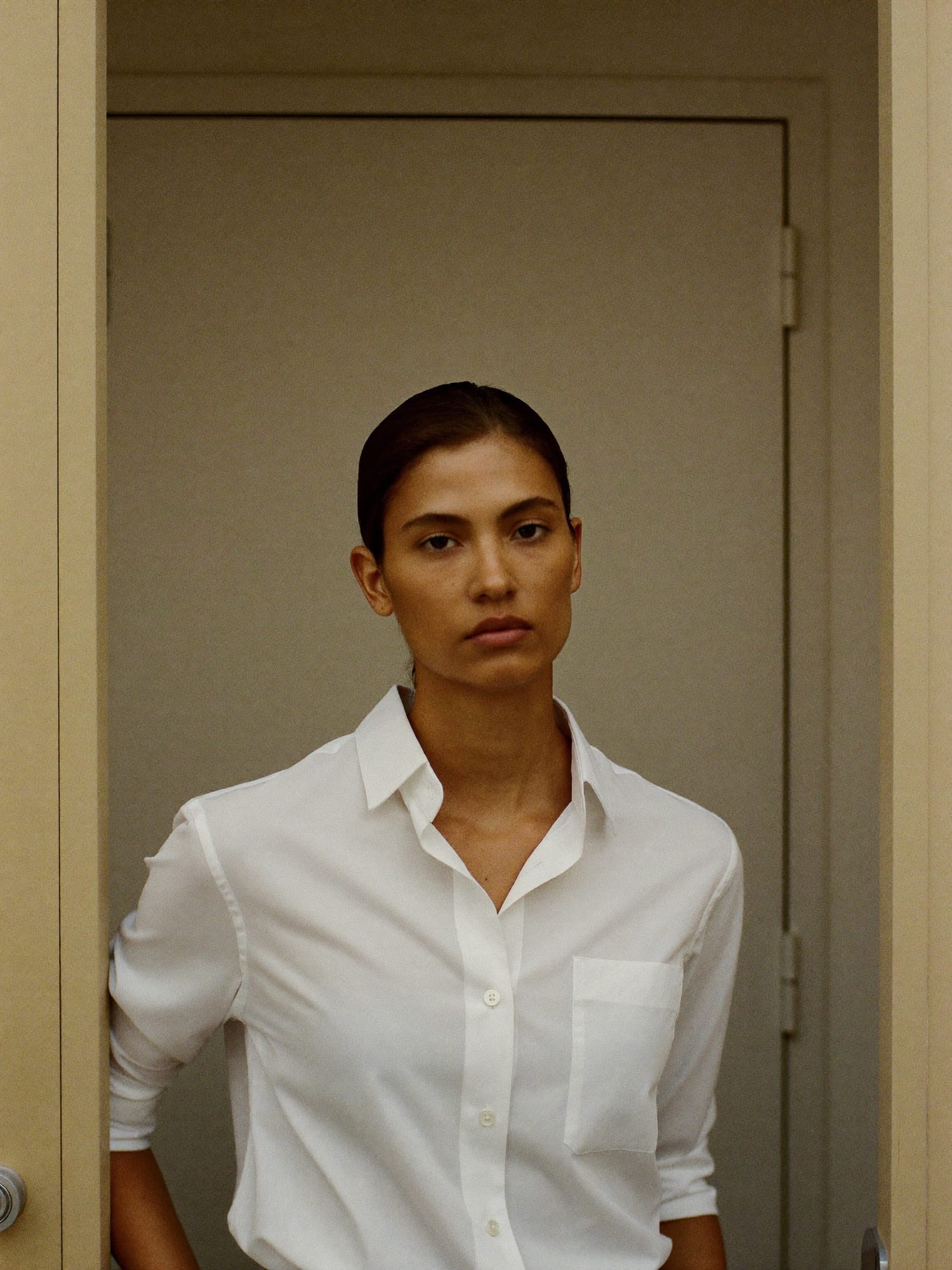A documentary portrait of a young professional woman in a white shirt, standing in a doorway